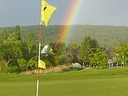 Markierung / Fahne auf dem Rasen vom Golfplatz - im Hintergrund ein Regenbogen am Himmel .