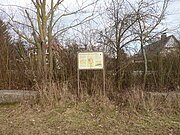 Vor einer Gruppe Büsche steht eine Informationstafel mit der Überschrift "Römisches Kastell".