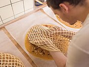 Person legt ein Gitter aus Teig über eine runde, ungebackene Torte auf einem Tisch in einer Küche.