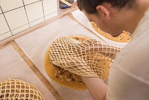 Person legt ein Gitter aus Teig &uuml;ber eine runde, ungebackene Torte auf einem Tisch in einer K&uuml;che.